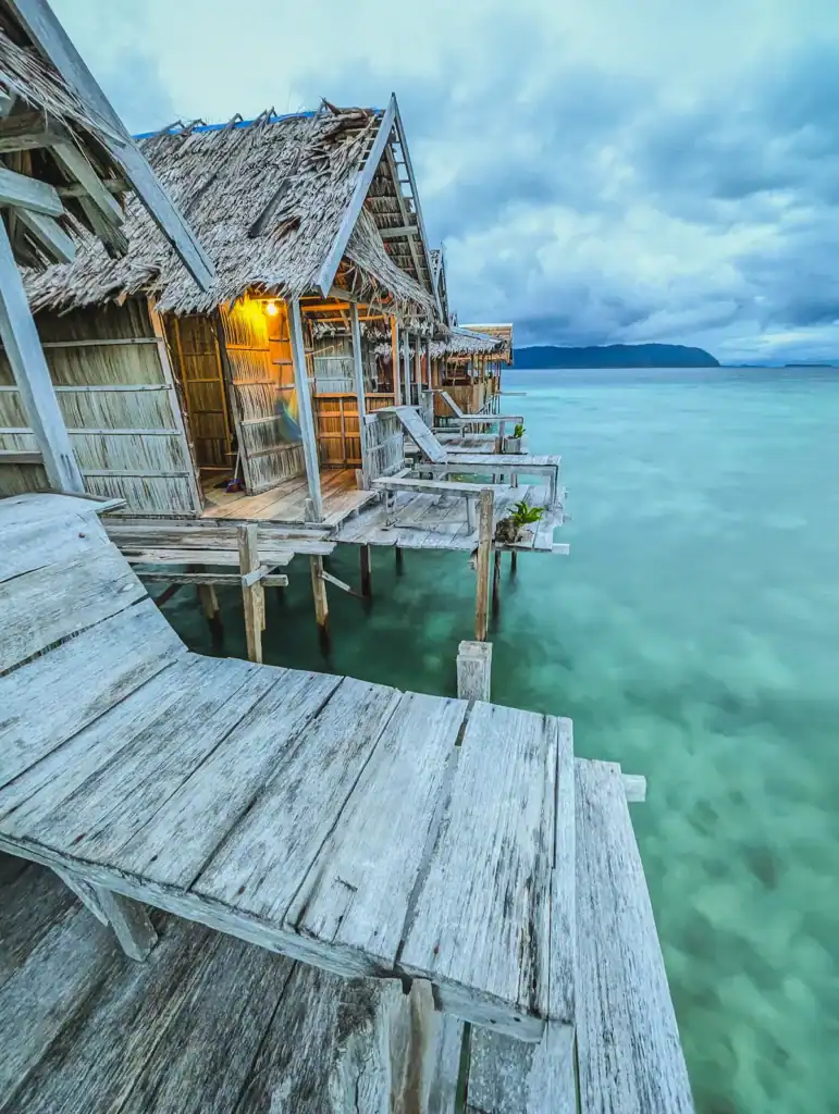Overwater bungalows on Arborek Island homestay in Raja Ampat at sunset, overlooking turquoise lagoon