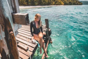 Scuba Diver sitting on wooden jetty above turquoise water at a homestay in Raja Ampat, Indonesia