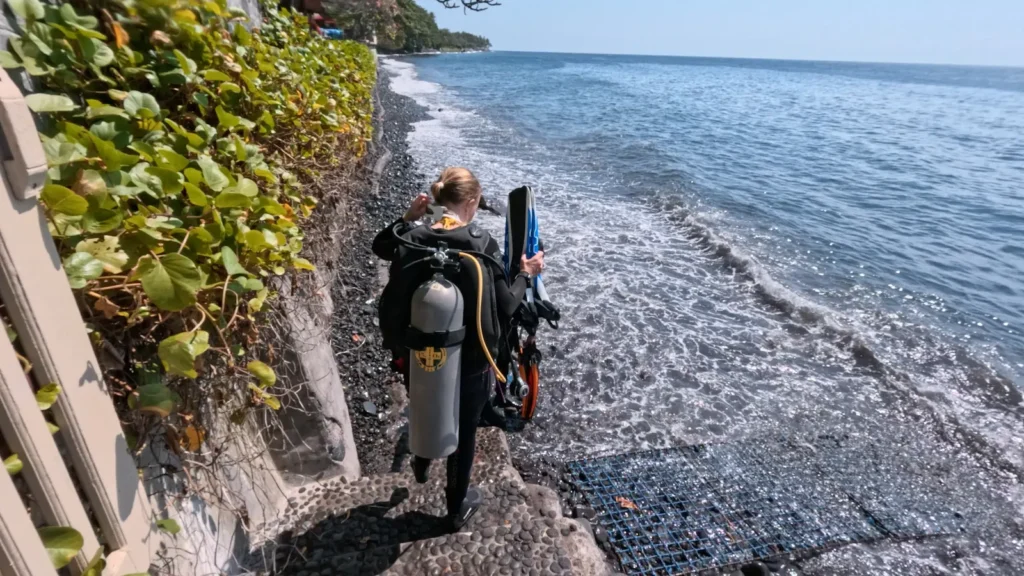 Scuba diver preparing to enter the water via the rocky volcanic shore at the USAT Liberty Wreck site.