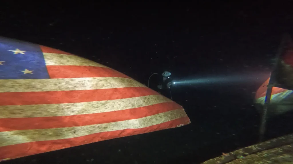 Diver illuminating the American flag marker on the USAT Liberty Wreck during a night dive in Tulamben, Bali.