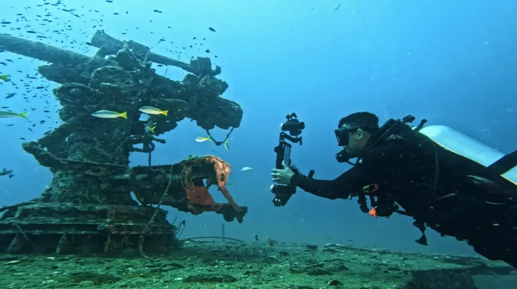Scuba diver swimming horizontally while filming a reef with an underwater camera rig
