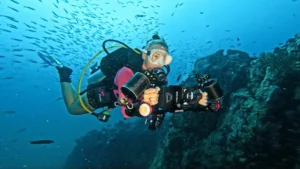 Scuba diver filming underwater with a dual-light camera rig, float arms and underwater housing
